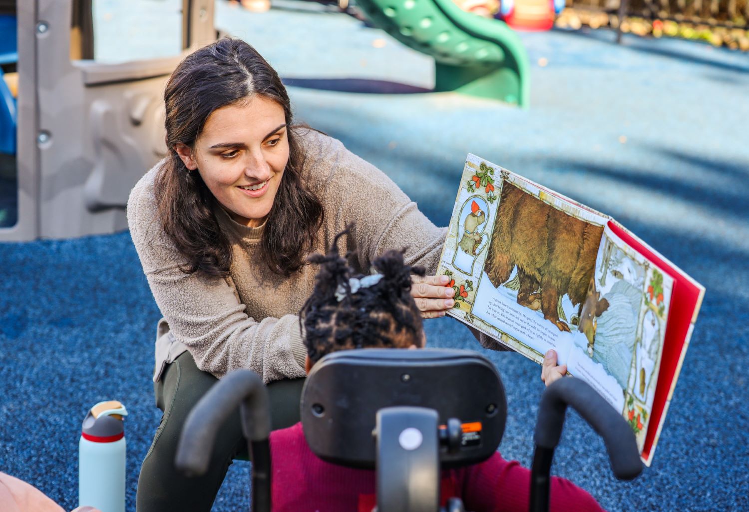 Photo of a staff member from The Therapy Place outdoors reading a children's book to one of their young clients.