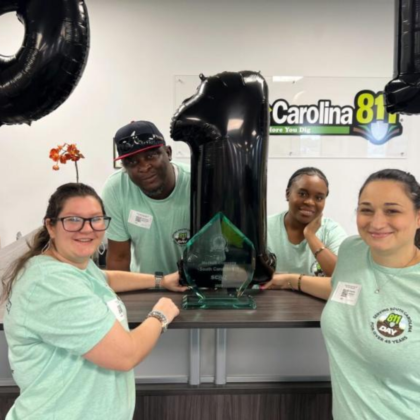 Group photo of South Carolina 811 staff members gathered around desk with inflated '811' balloons around them