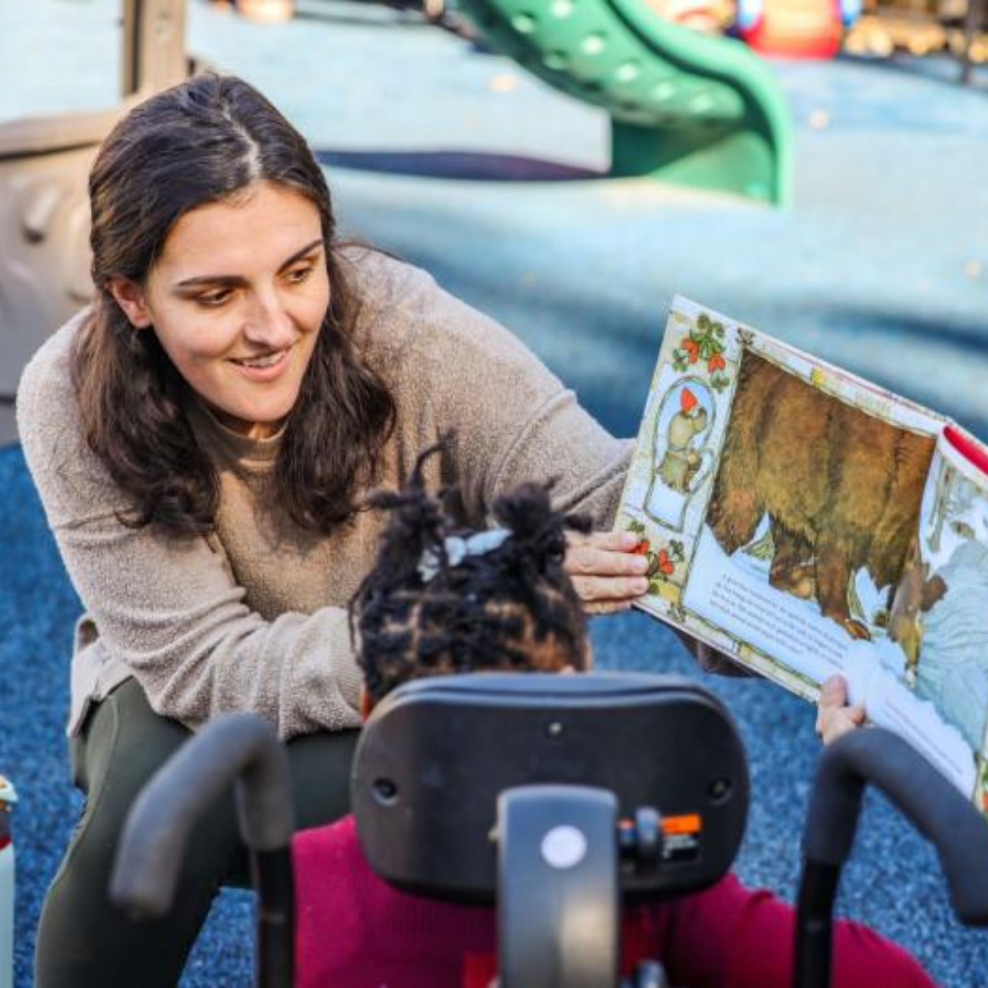 Photo of a staff member from The Therapy Place outdoors reading a children's book to one of their young clients.