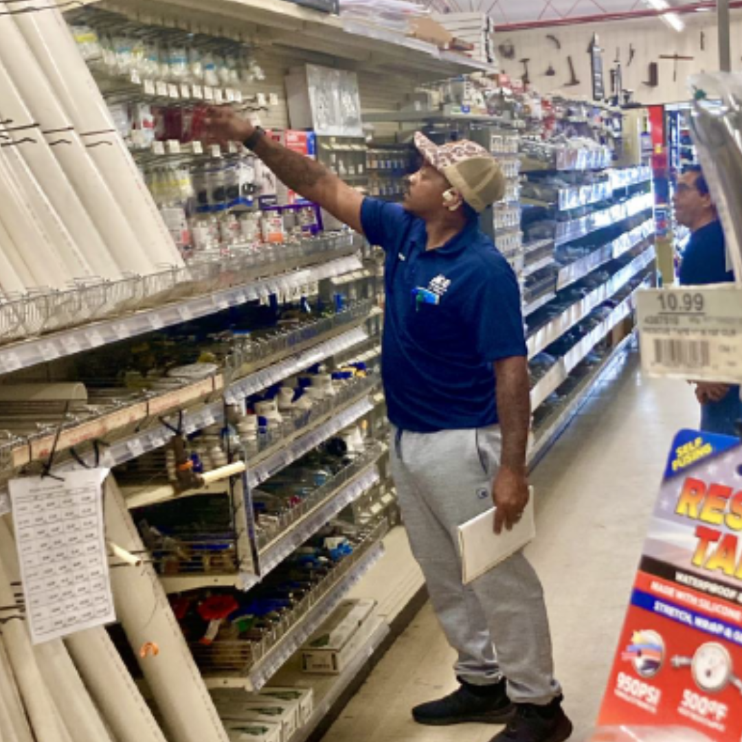 Ace Hardware worker is working, lifting his arm up to grab an item from the racks