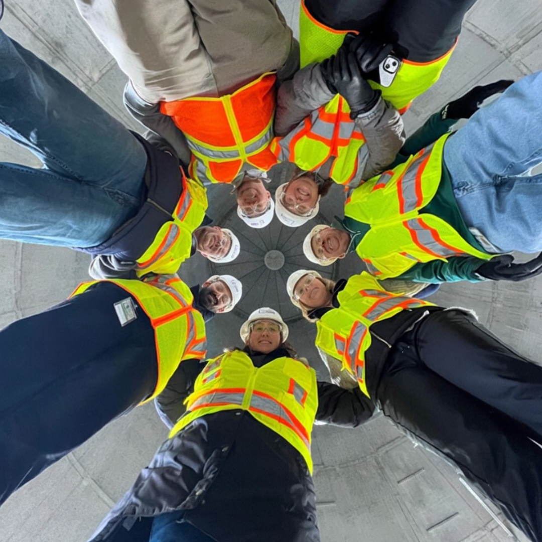 Seven workers for Beaufort- Jasper Water and Sewer Authority are standing in a circle above the camera, looking down, they're all in yellow and orange reflective vests 