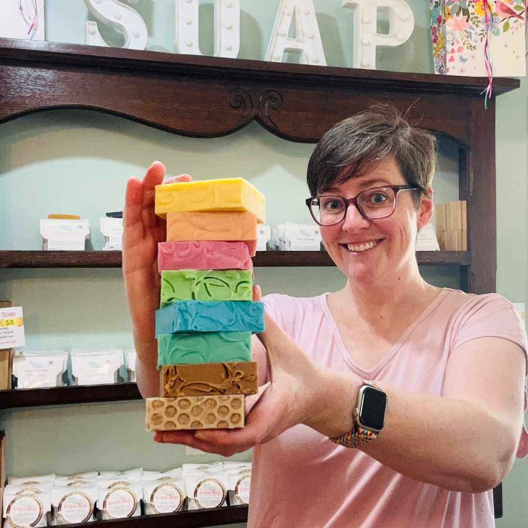 A woman is holding 8 bars of soap, stacked on top of one another, posing for the picture