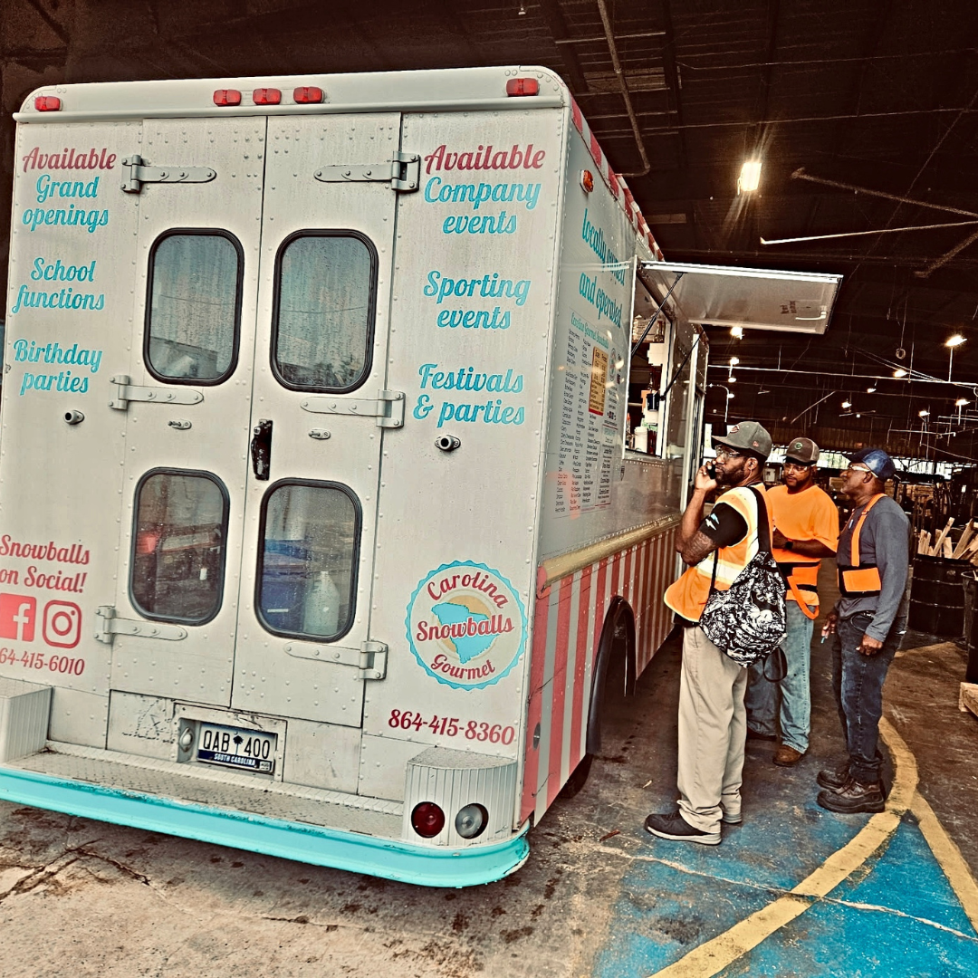 Three men, all in reflective gear, are standing in front of a Carolina Snowballs truck, about to order