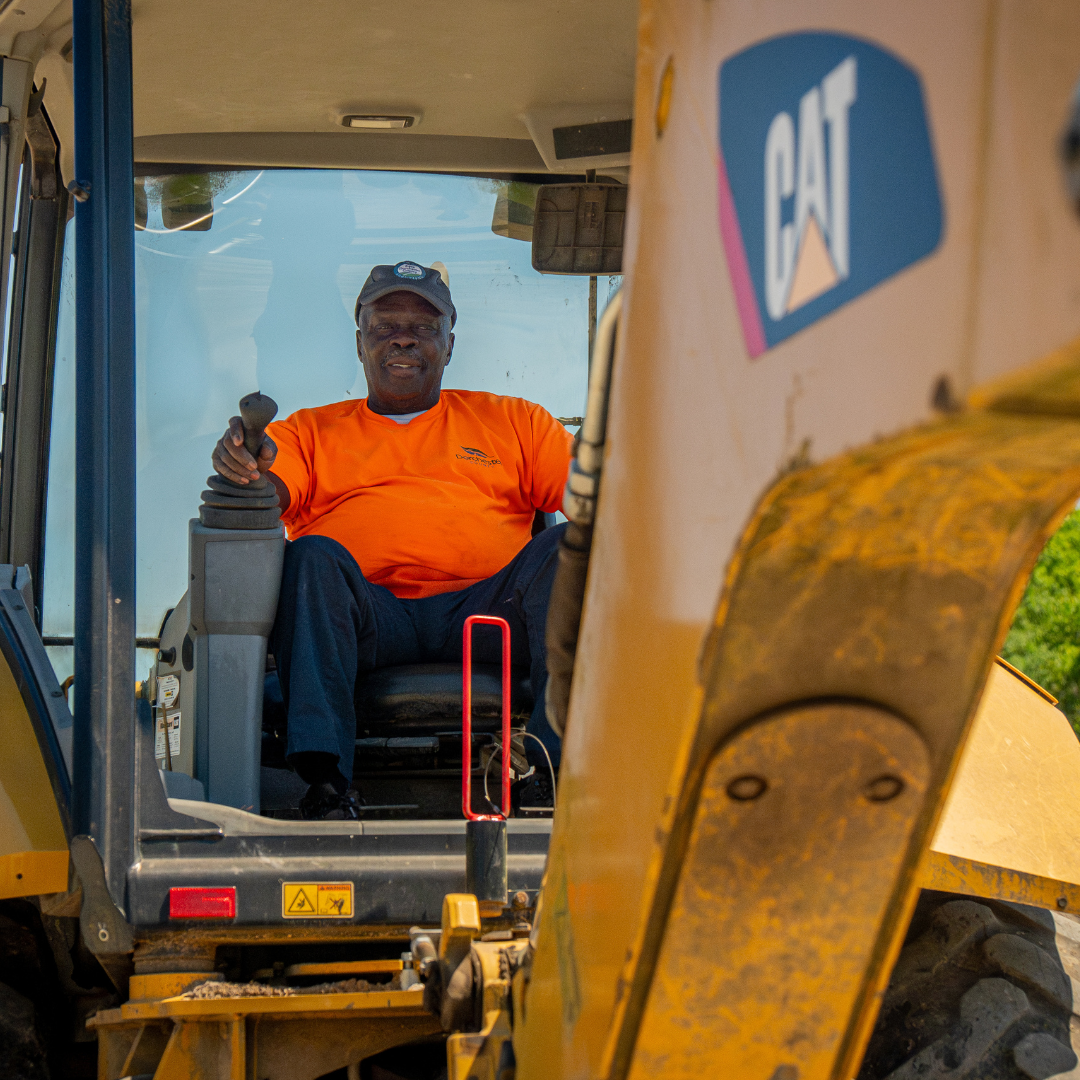 A man in a bright orange shirt is sitting, operating an excavator