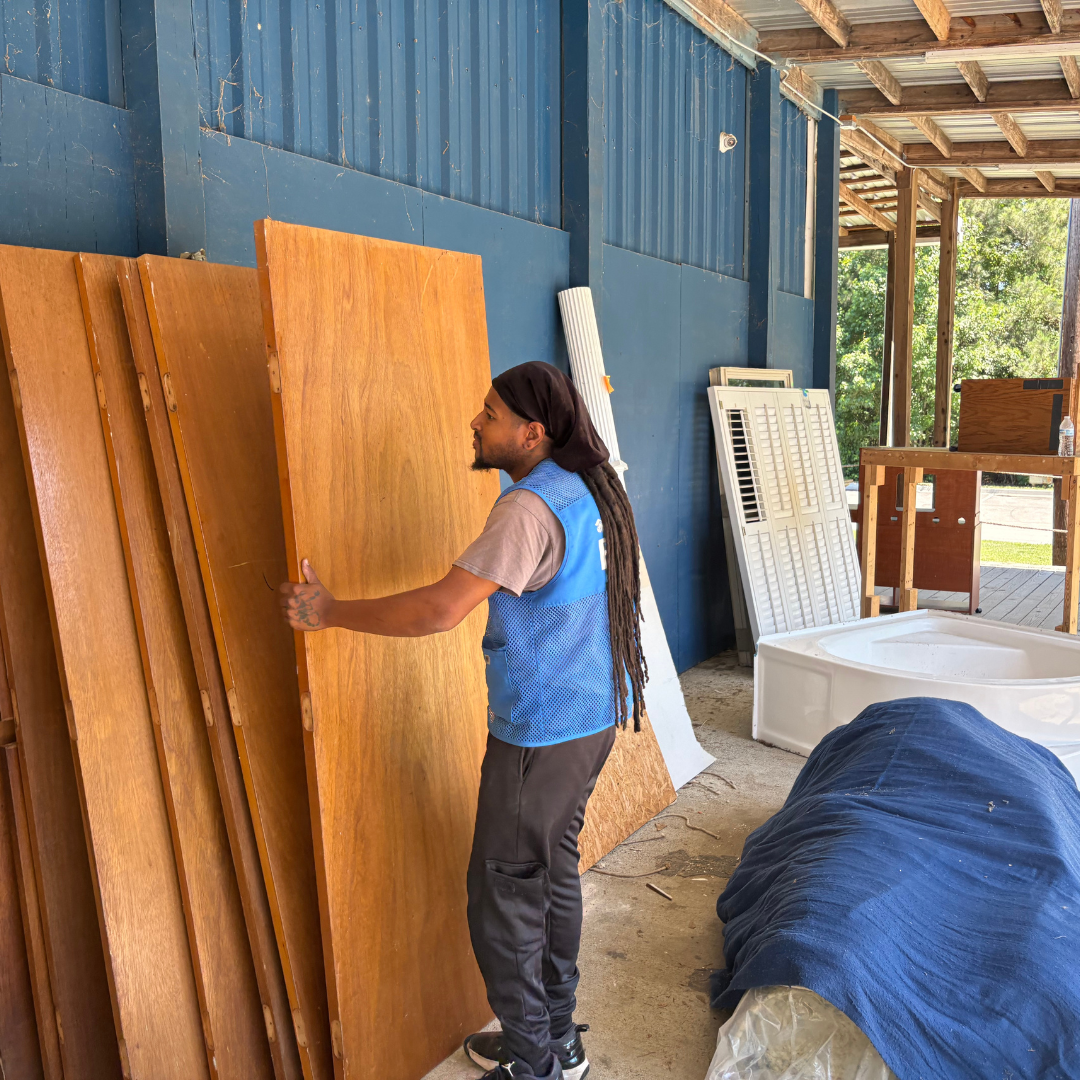 One man appears in front of several wood slats, doors without hinges, attempting to lift one up to move
