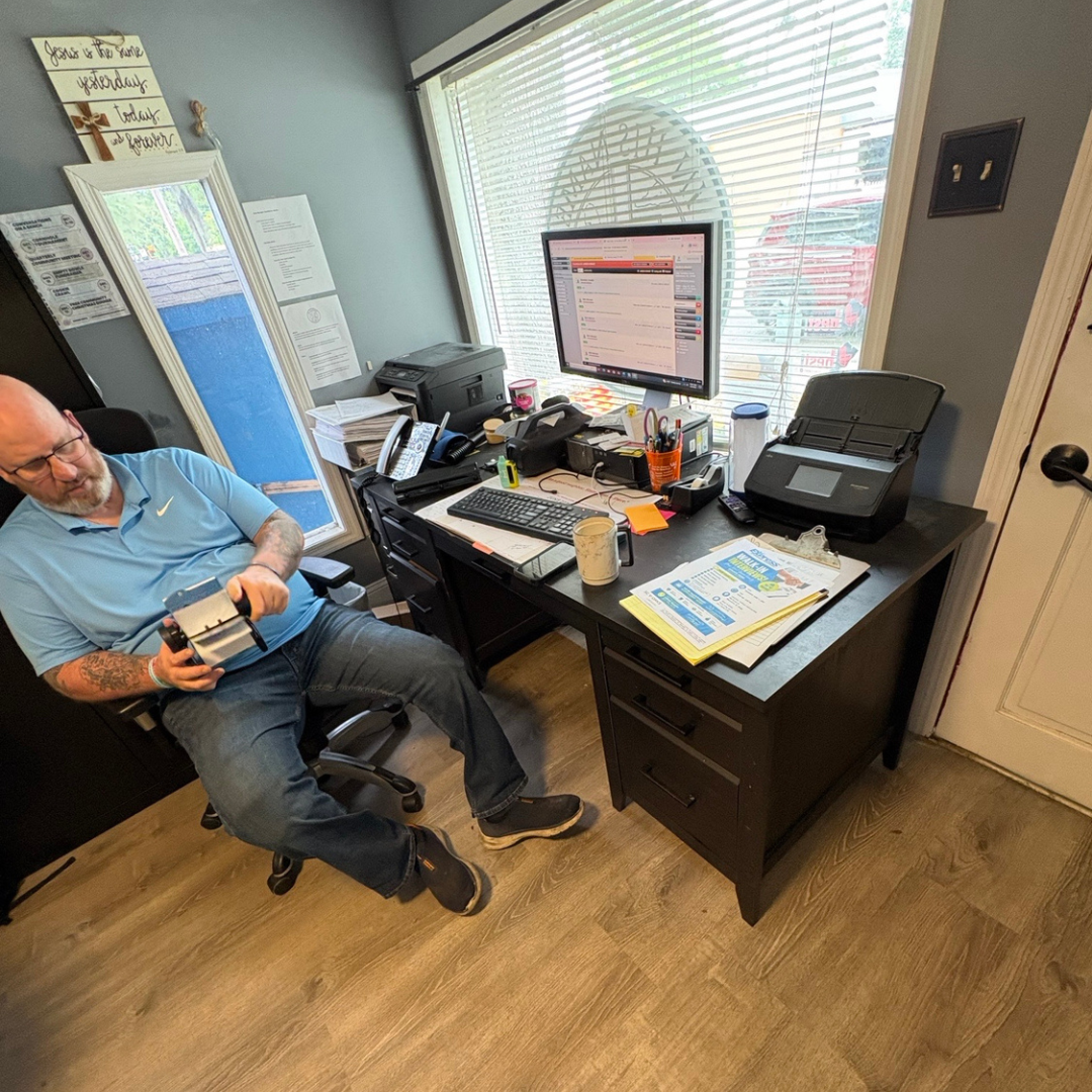 A man sits at his chair near his desk, looking at a calendar while he works