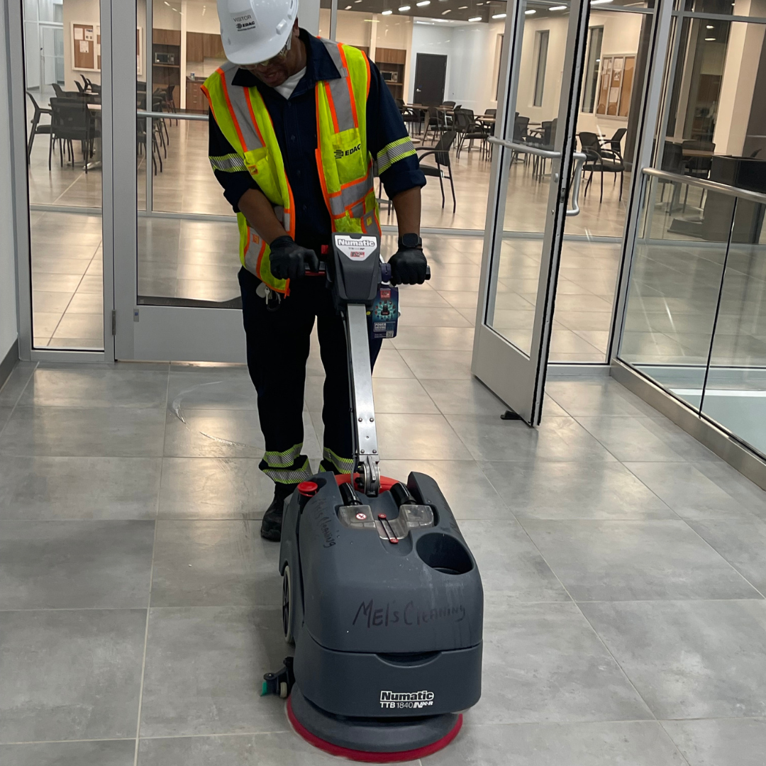 A man in a reflective vest and hard hat uses a cleaning machine to buff the floors