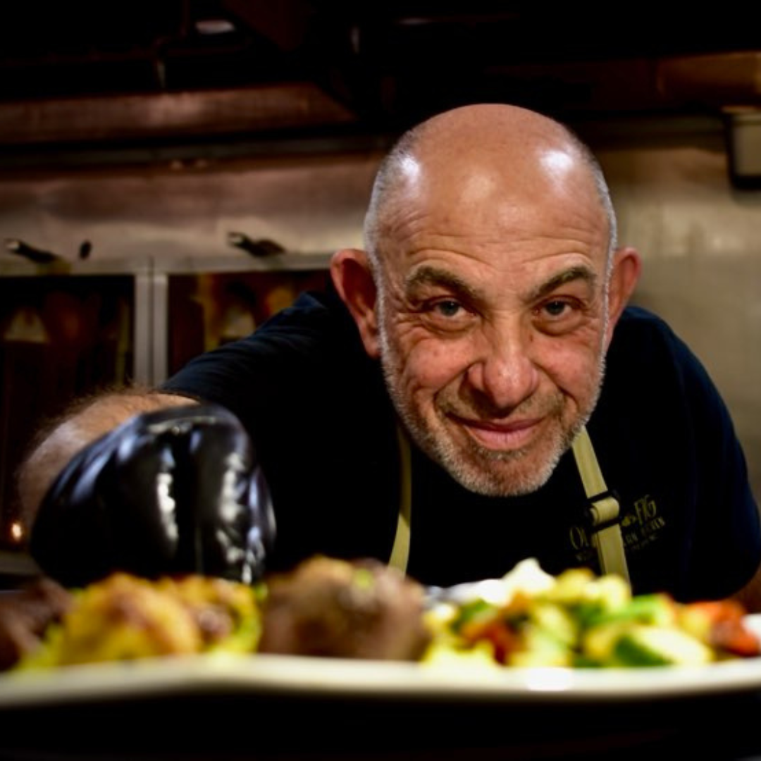 A chef working in the kitchen is up close to the camera, presenting the plate with food on it 