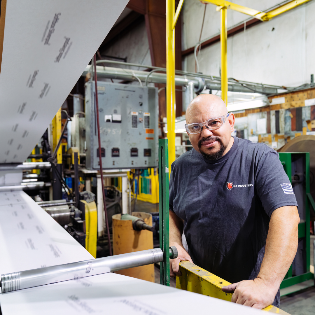 A man with protective glasses looks towards the camera as he is next to machinery 
