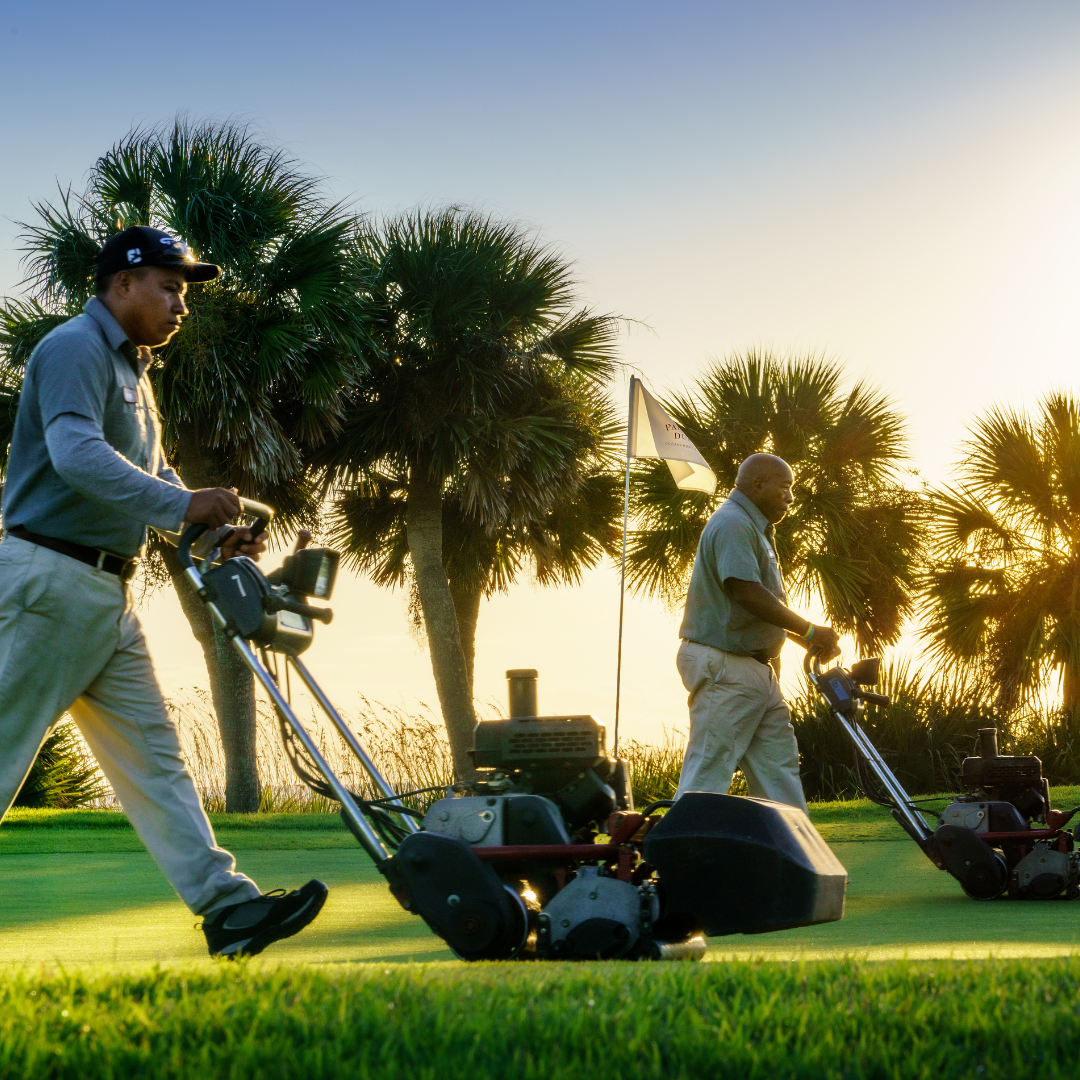 Two workers use a lawn mower to make a golf course hole presentable 