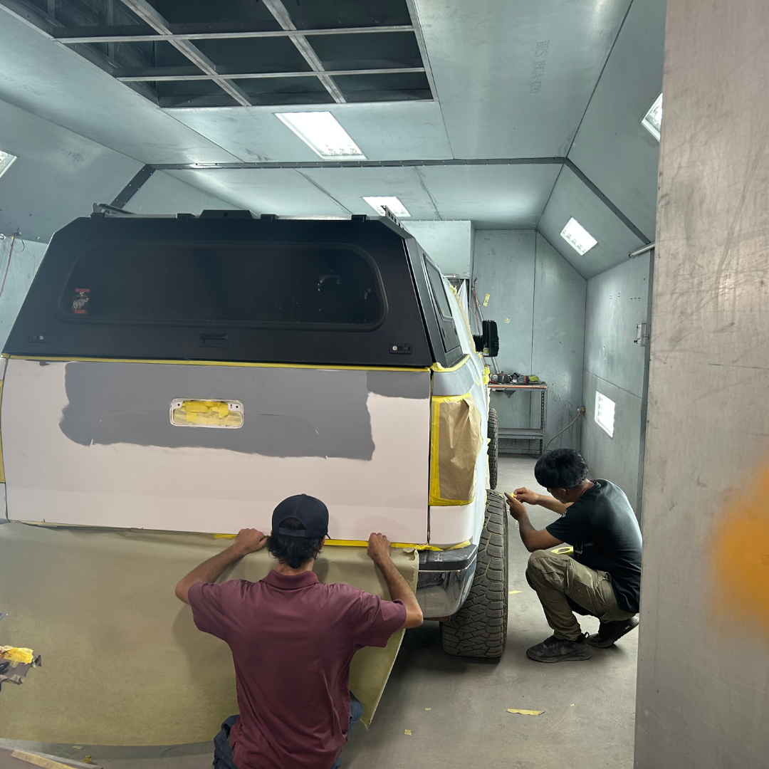 A man works behind a white vehicle, working to paint the back of it 