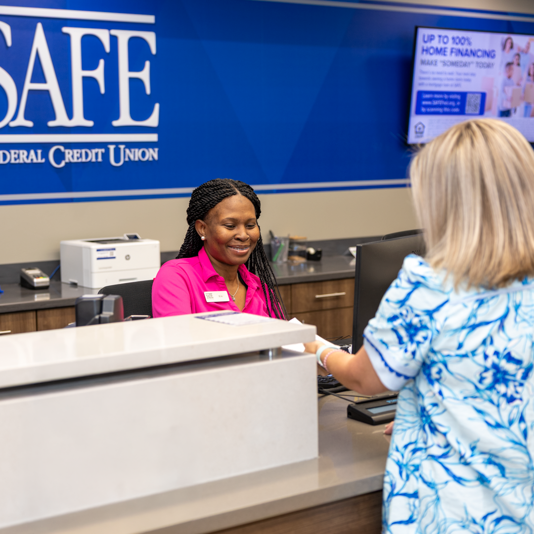 A woman works behind a teller booth, assisting a woman trying to receive service from the bank