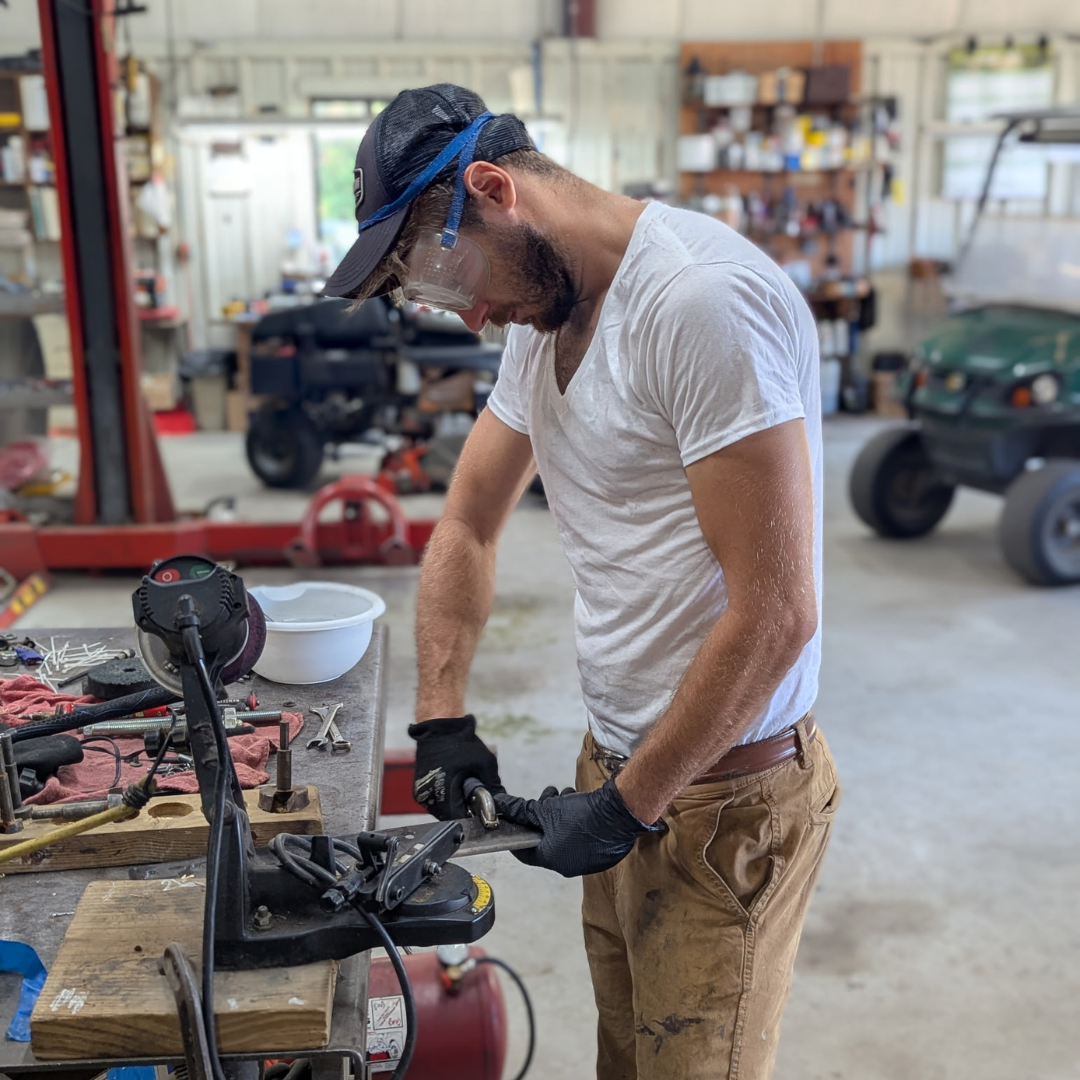 A man works with protective glasses to mend a piece of medal with tools 