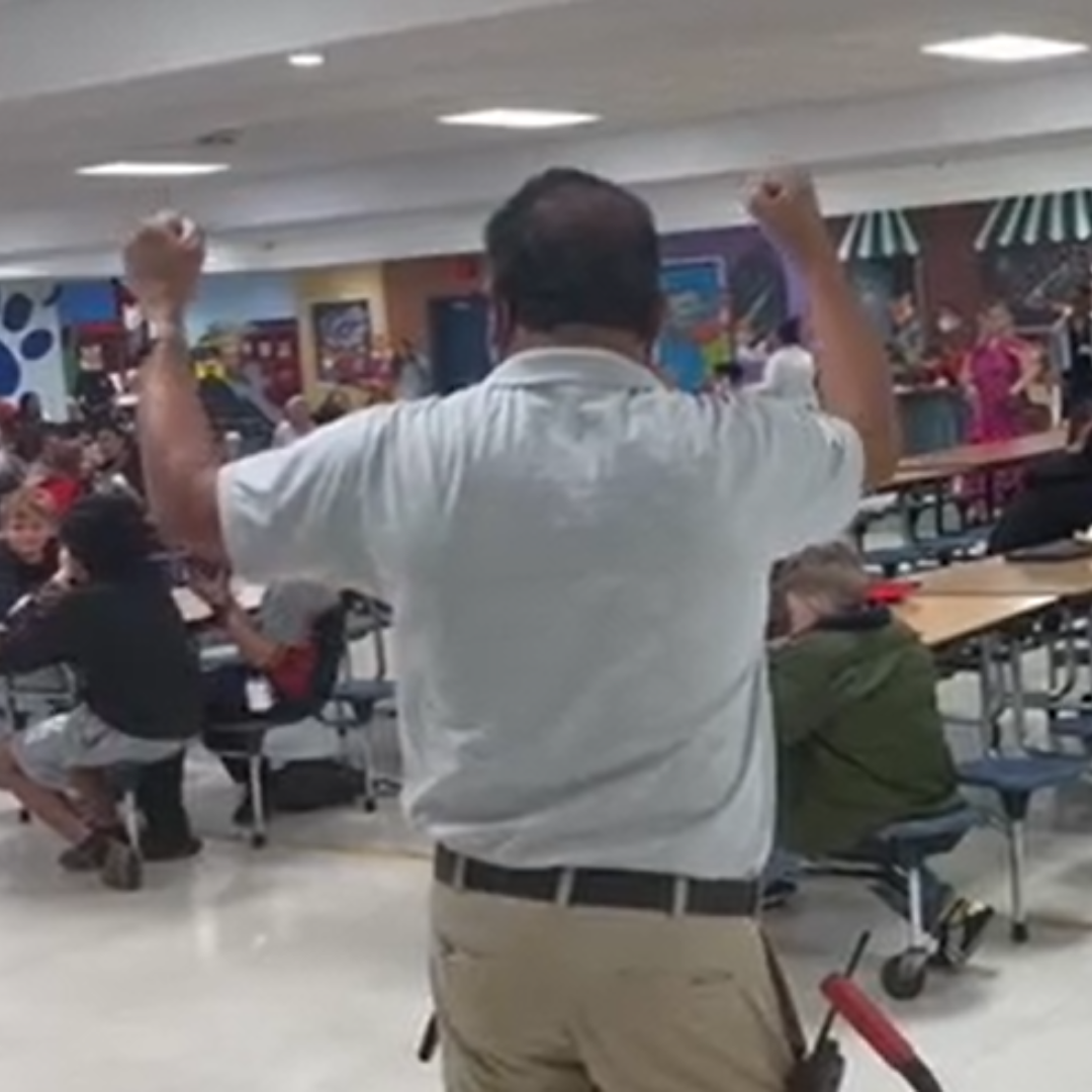 A man looks out to a cafeteria, with his hands in the air