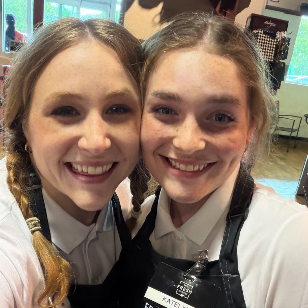 Two Fresh Market workers put their heads together and smile at the camera for the picture