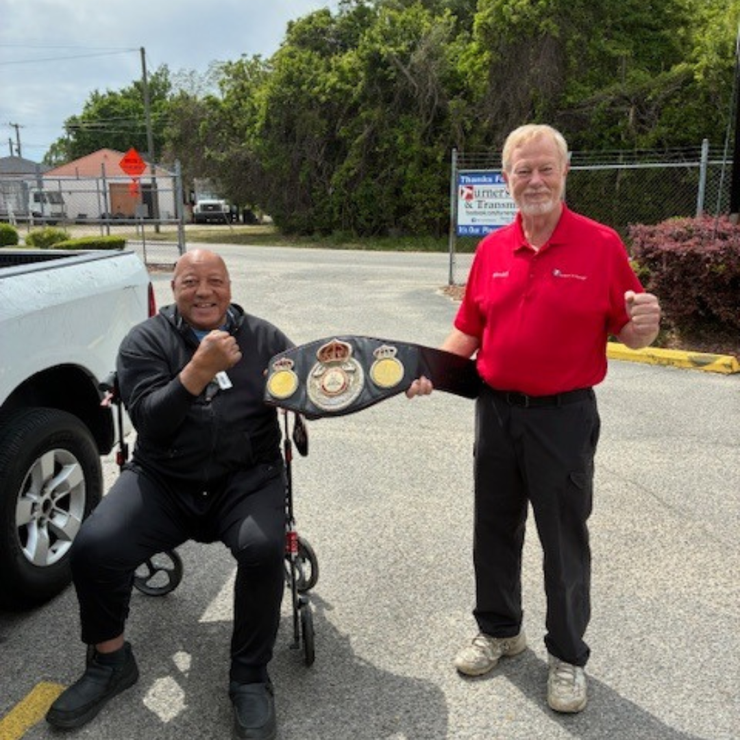 A man in a red shirt holds one end of a belt with another man in a wheelchair to his right 