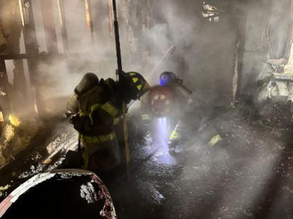 Two firefighters stand in the middle of a smoke cloud, which filled a burned-down room. Wall framing is visible.