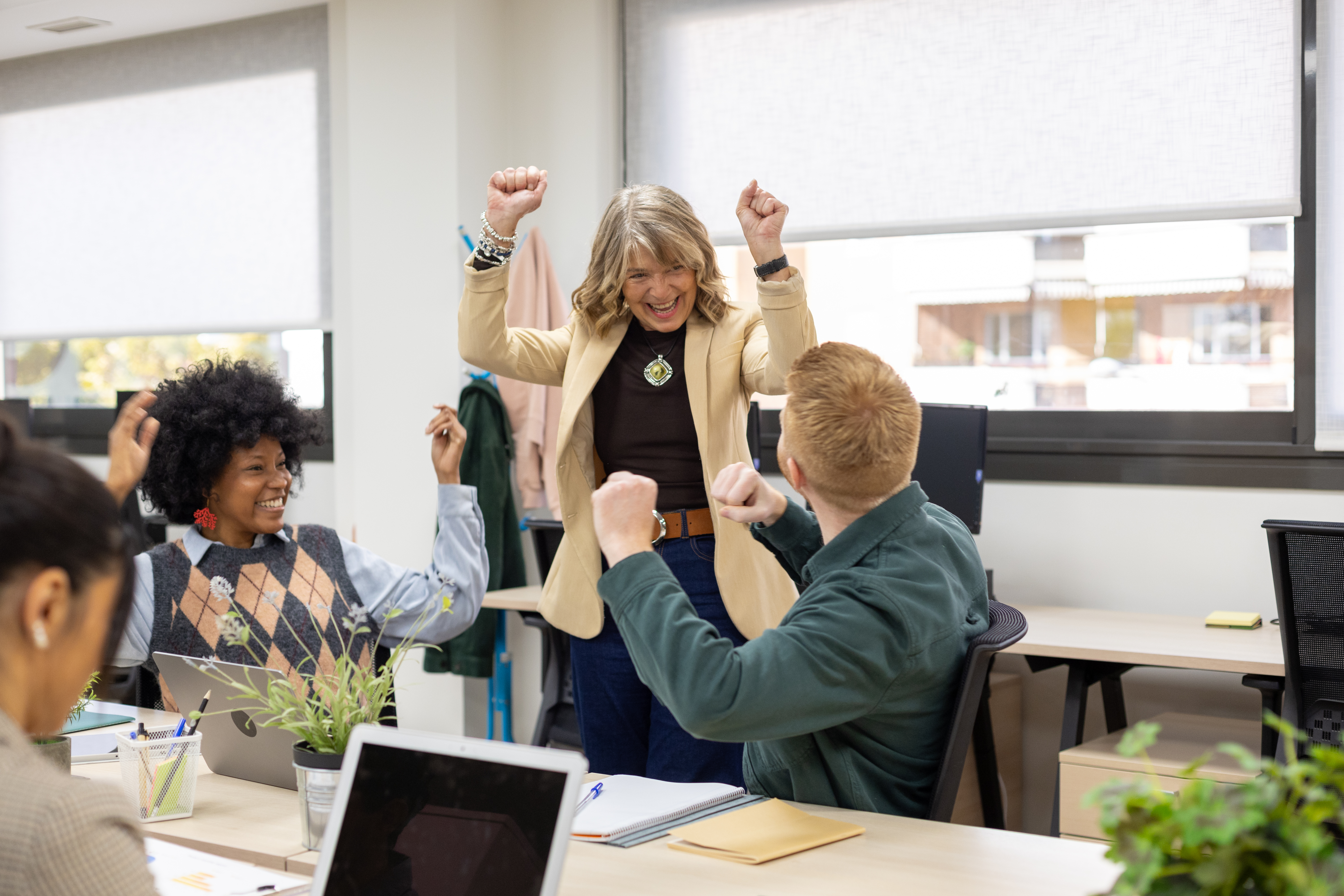 Celebrating World Productivity Day. The picture features three people, working in an office setting, with their hands raised.