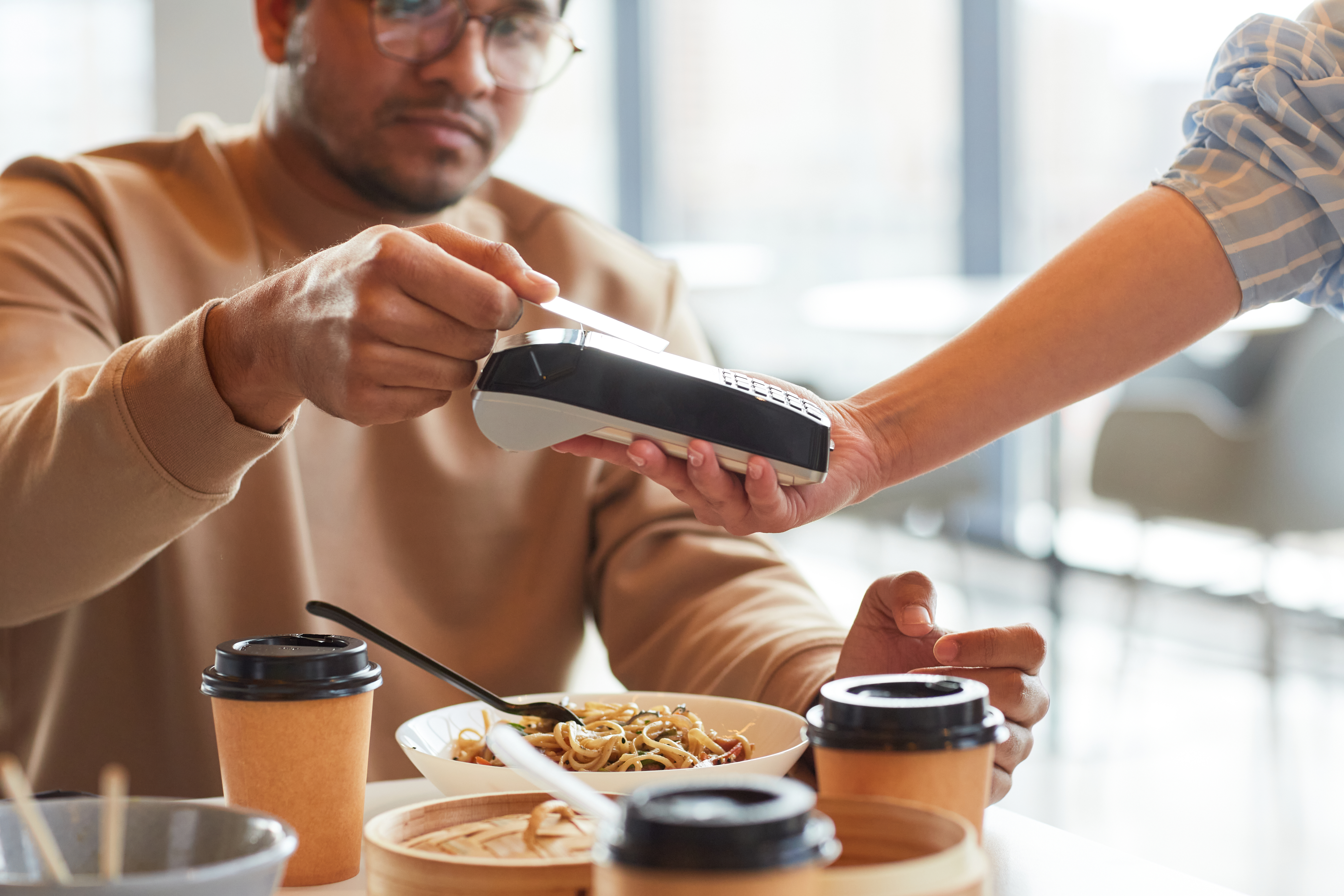 A man is paying with his credit card. There is a bowl of pasta and three coffee cups on the table.