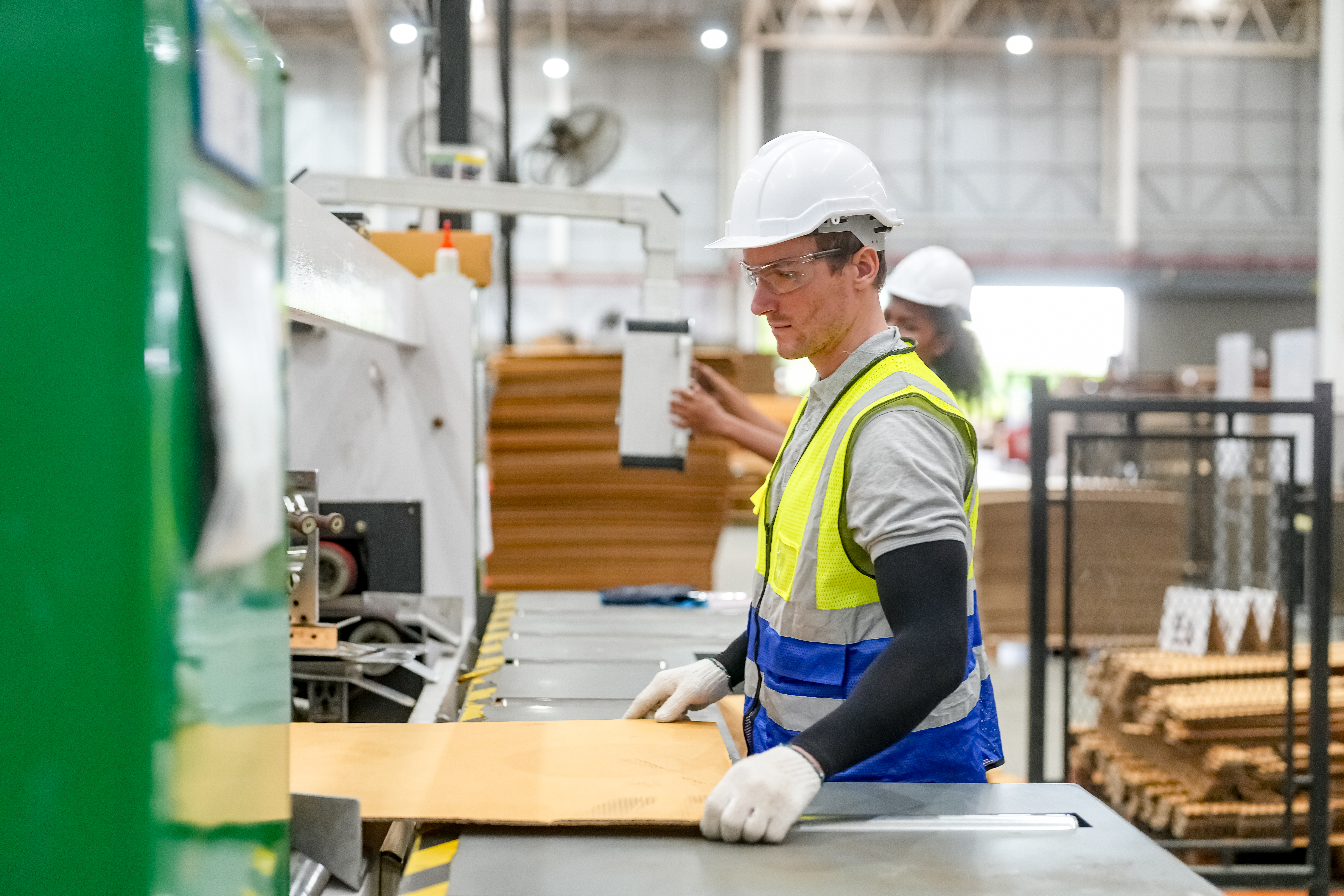 A man wears safety glasses, white gloves, and a safety vest while working on an assembly line.
