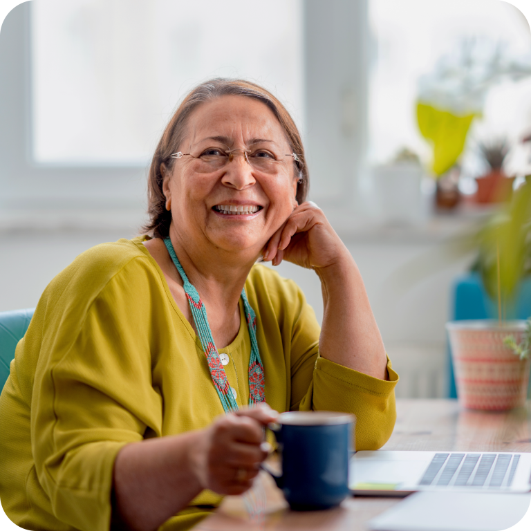 Woman smiling and sitting in front of a laptop on a desk.