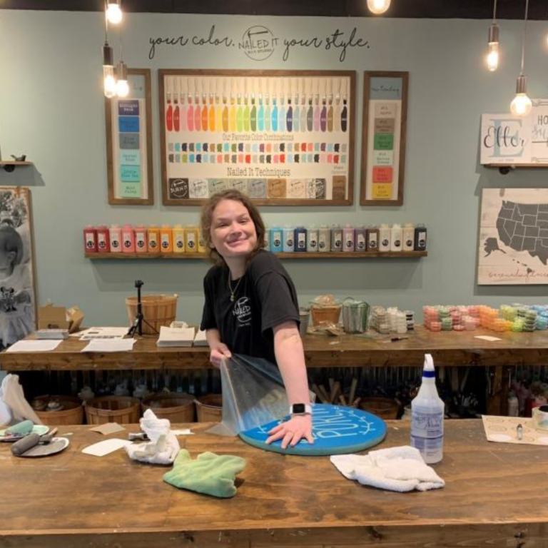 Staff member smiling at camera as she unwraps crafted sign at studio work table