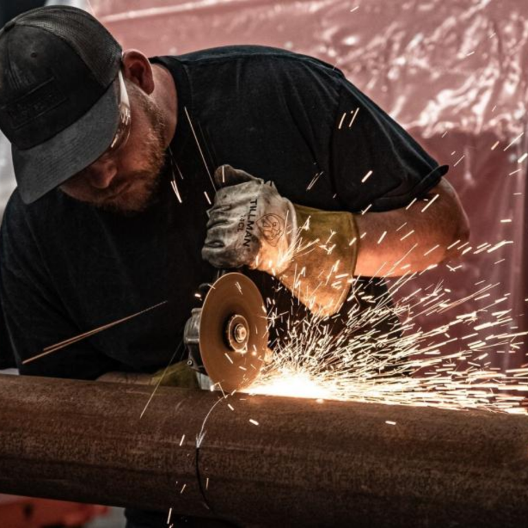 Photo of WEIMA staff member cutting a metal piece with handsaw-type tool, causing sparks to fly off metal piece