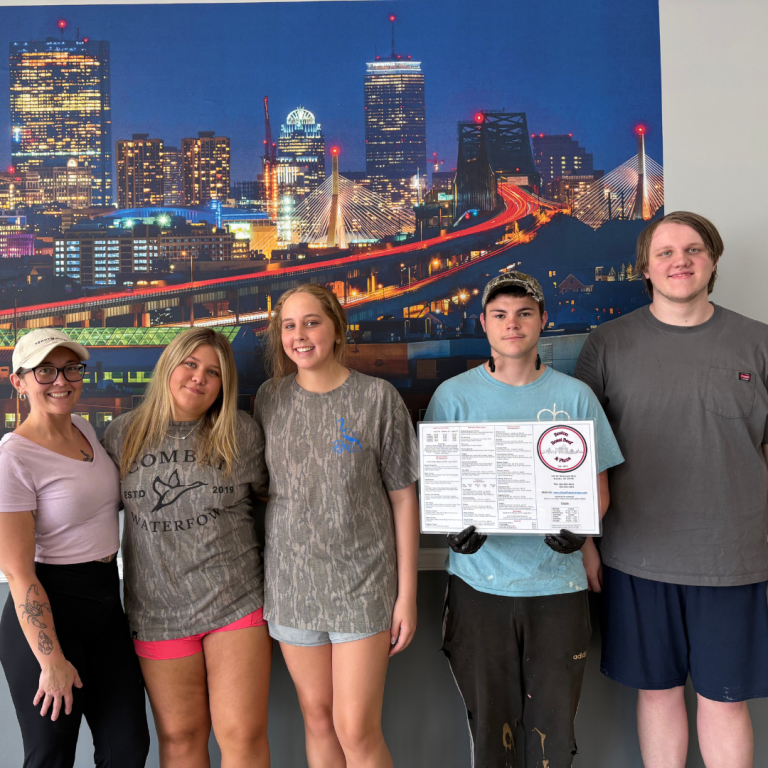 Three female, and two male workers are standing in their place of work against a wall, holding a menu, posing for the picture
