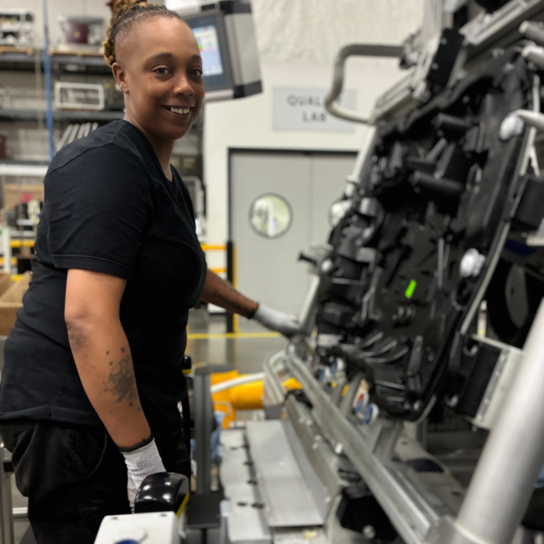 A woman is standing in front of machinery in all black, smiling for the picture 