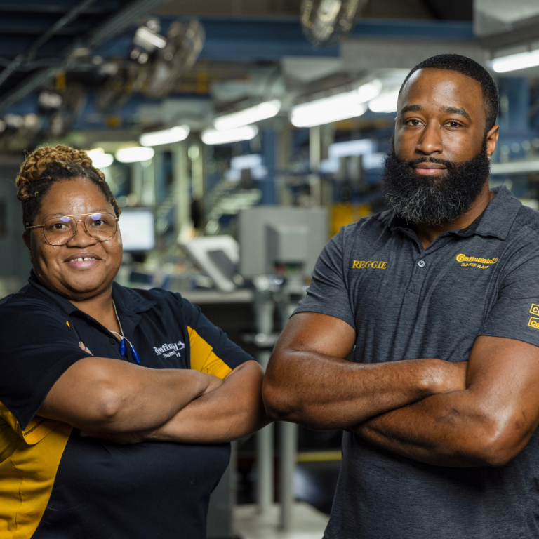 Two individuals, one man, and one woman, are arms crossed, standing next to each other, wearing Continental Tire Sumter Plant shirts