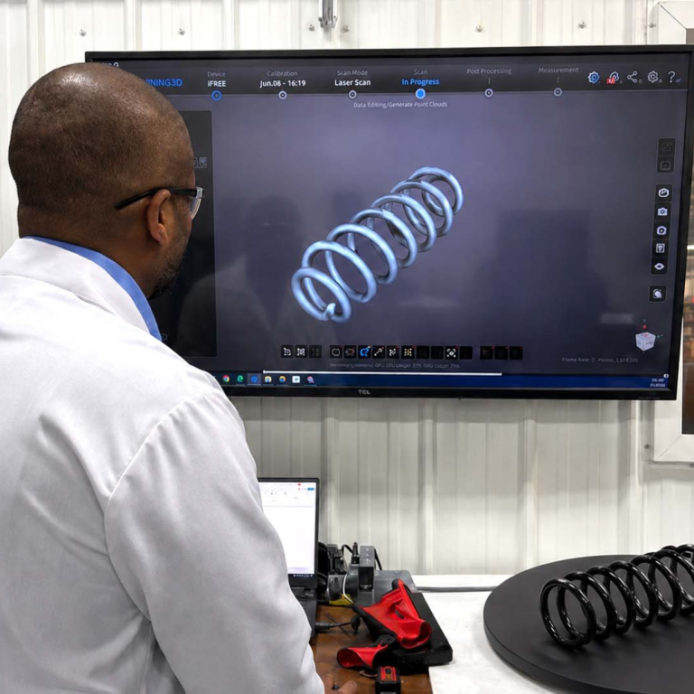 A man in a white lab coat is looking at a mounted television, viewing a coiled spiral on the screen 