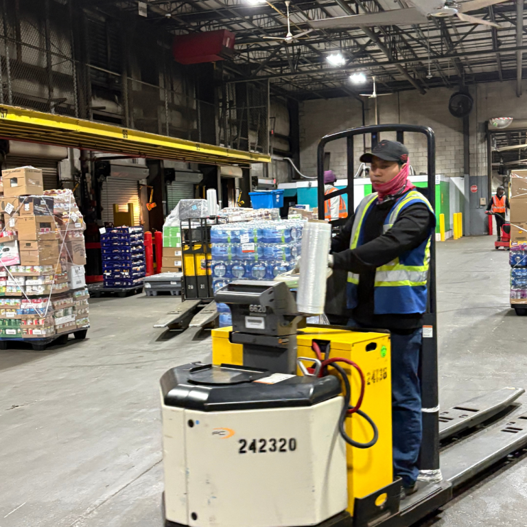 A man in reflective clothing a face mask is on a reach extender, operating the machine