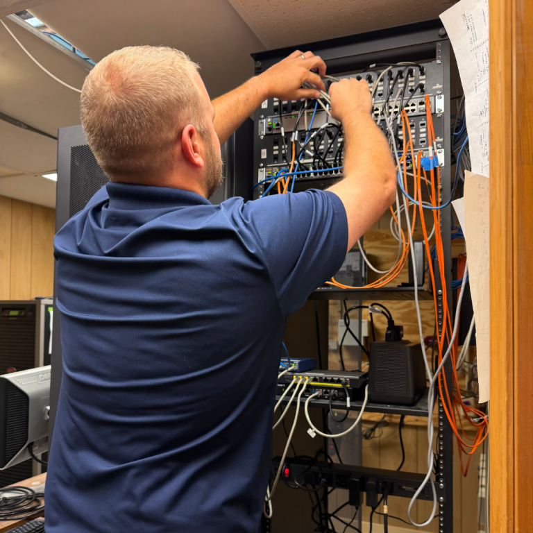 A man works to fix a telephone line with a lot of colored wires coming out of a wall 