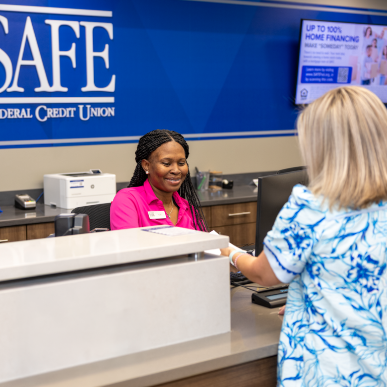 A woman works behind a teller booth, assisting a woman trying to receive service from the bank