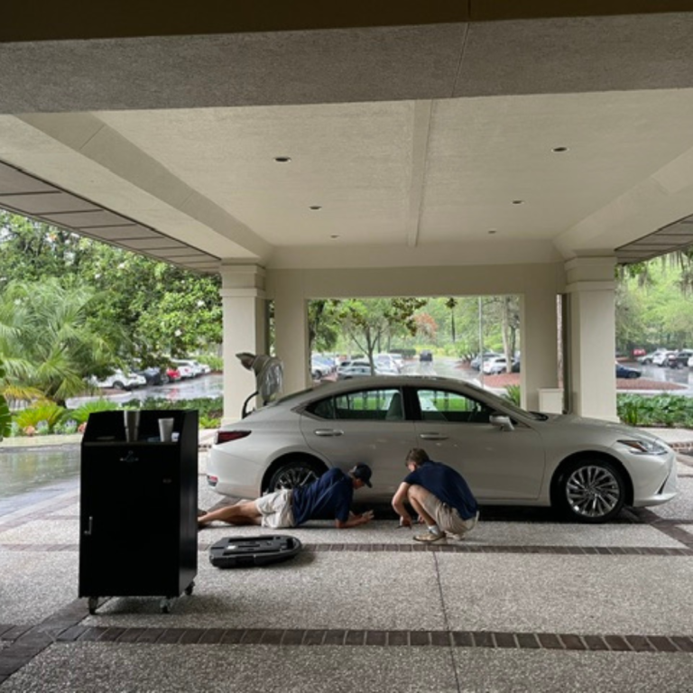 Two men work under a covered path, fixing a car