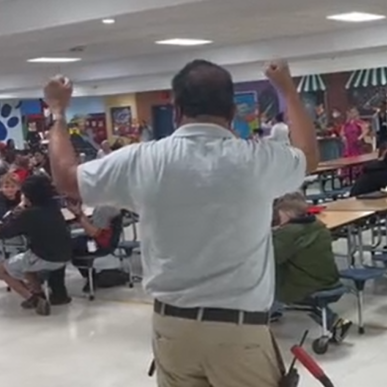 A man looks out to a cafeteria, with his hands in the air